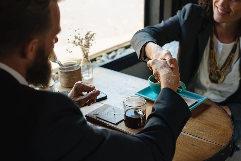 Business man and woman shaking hands while seated at a table.